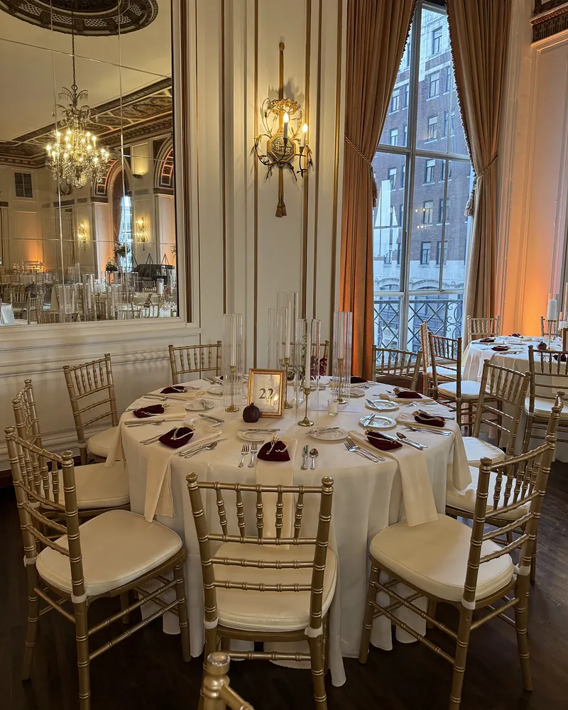Ballroom set with gold chairs, ivory linen and candlelit tables beneath a chandelier