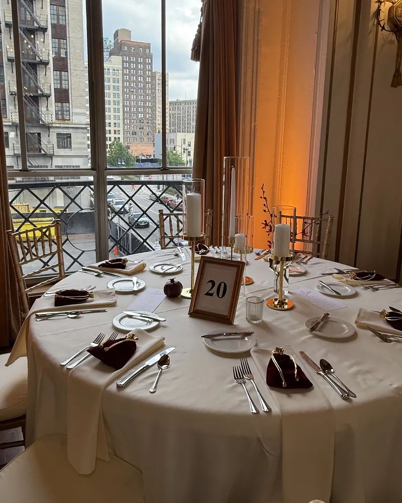 Round table with burgundy napkins, gold candleholders and a framed table number by tall windows